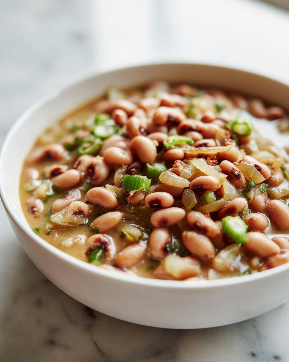 Close-up of a white bowl filled with a hearty blackeyed pea recipe, garnished with green onions and onions.