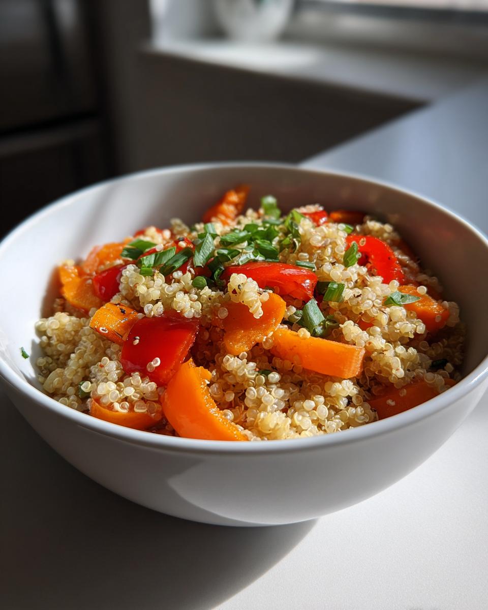 A white bowl filled with a healthy quinoa bowl featuring colorful bell peppers and carrots, garnished with green onions.
