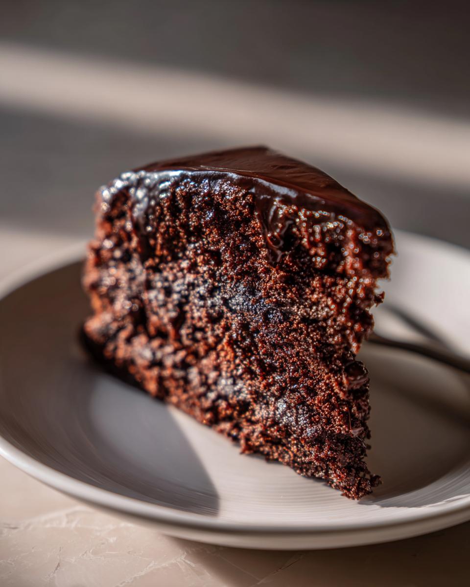 A close-up of a rich, moist slice of chocolate cake with glossy chocolate frosting.
