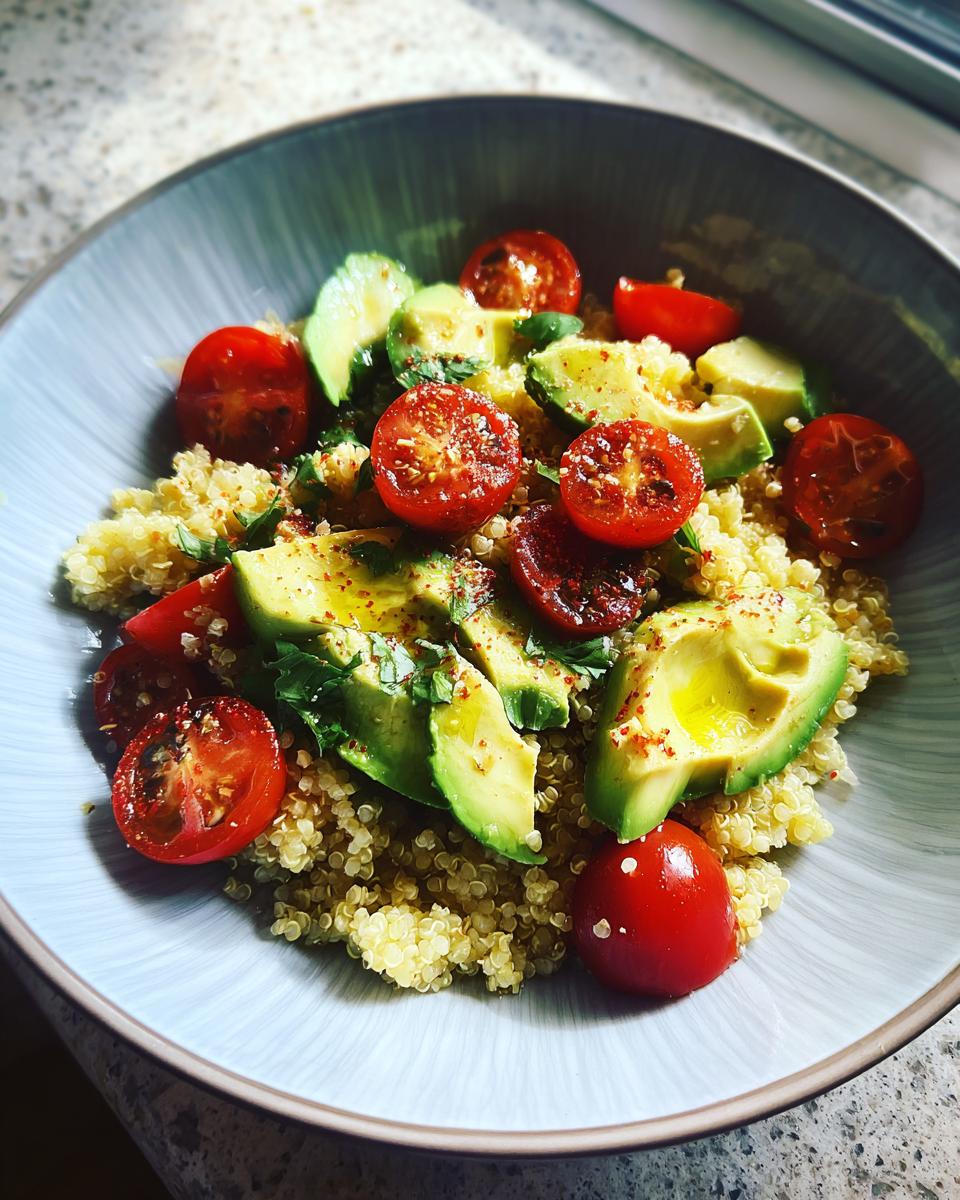A vibrant quinoa salad topped with sliced avocado, halved cherry tomatoes, and fresh herbs, showcasing a beautiful cooking aesthetic.
