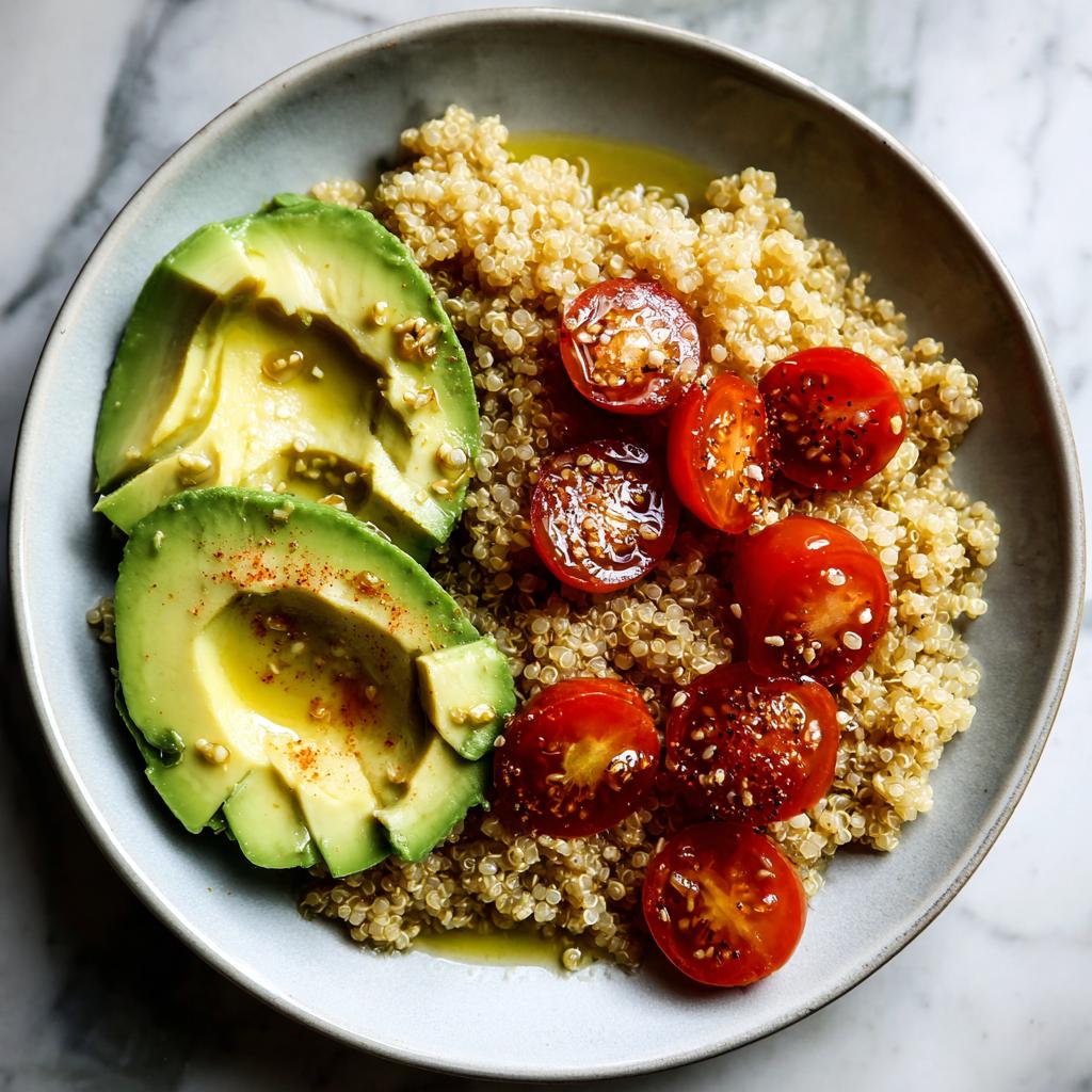 A vibrant quinoa bowl featuring sliced avocado, halved cherry tomatoes, and a drizzle of olive oil, showcasing cooking aesthetic.