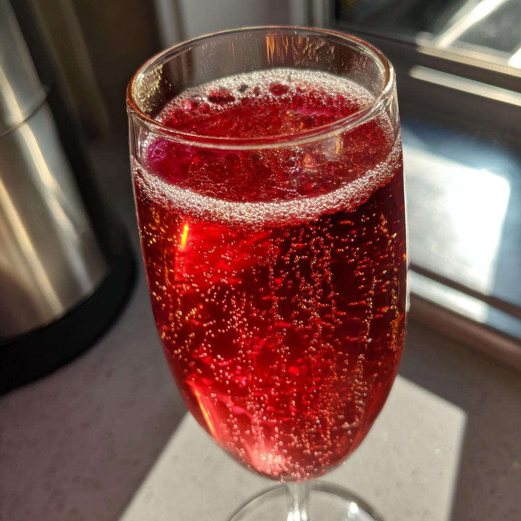 Close-up of a vibrant red NYE cocktail with effervescent bubbles in a champagne flute.