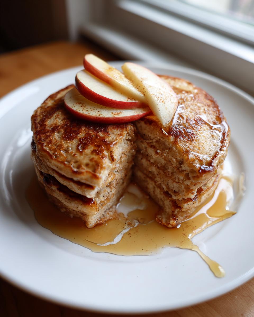 Stack of apple cinnamon protein pancake breakfast topped with sliced apples and drizzled syrup
