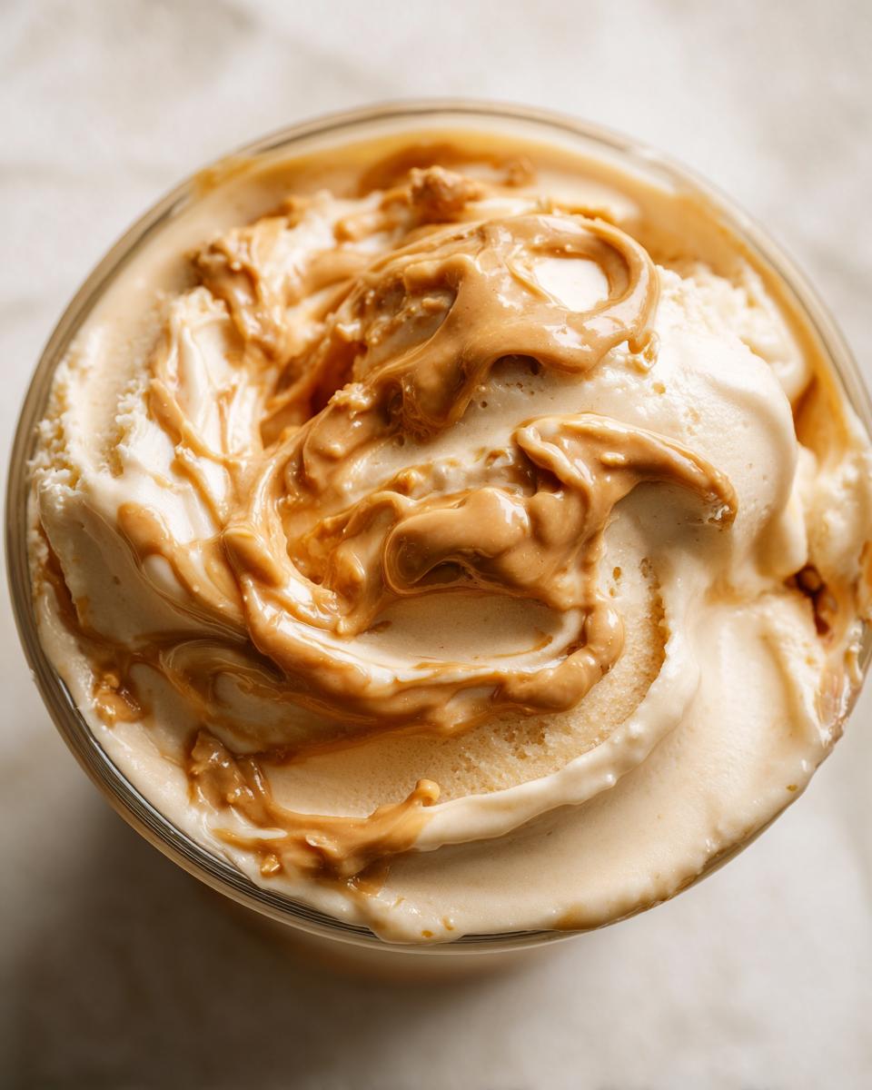 Close-up of banana nice cream with a peanut butter swirl on top in a glass bowl.