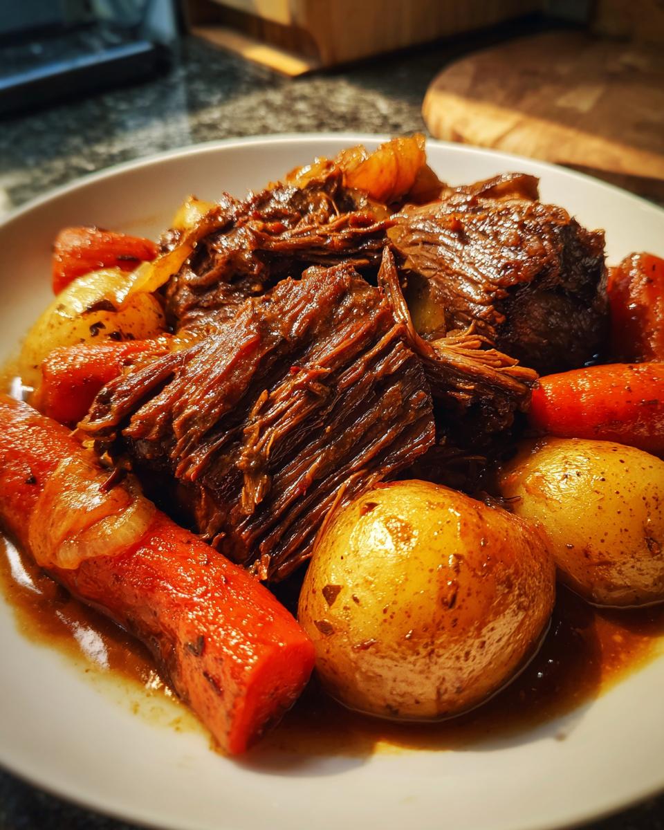 Plate of beef pot roast with tender carrots, potatoes, and onions in rich gravy.