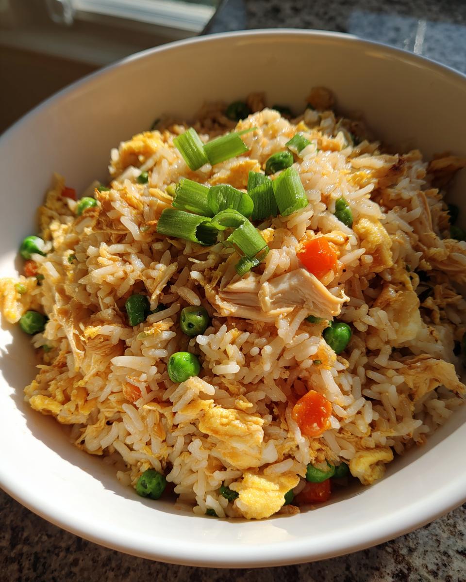 Close-up of chicken fried rice with peas, carrots, eggs, and green onions in a white bowl.