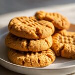 Close-up of a stack of golden flourless peanut butter cookie recipe cookies with one cookie partially broken.