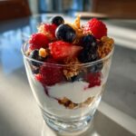 Glass of greek yogurt berry parfait dessert with strawberries, blueberries, granola, and yogurt layers.