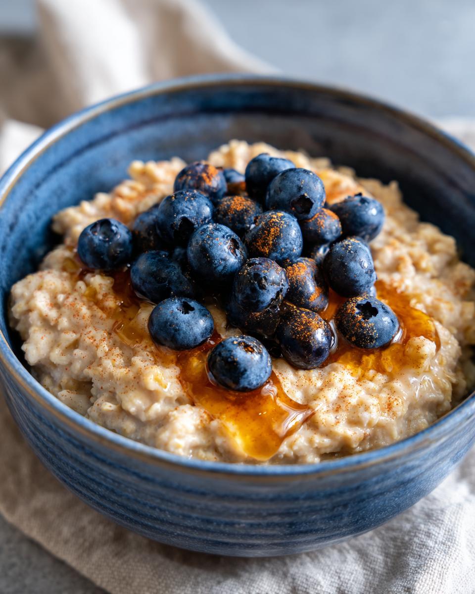Bowl of high protein blueberry oatmeal breakfast topped with fresh blueberries and honey drizzle