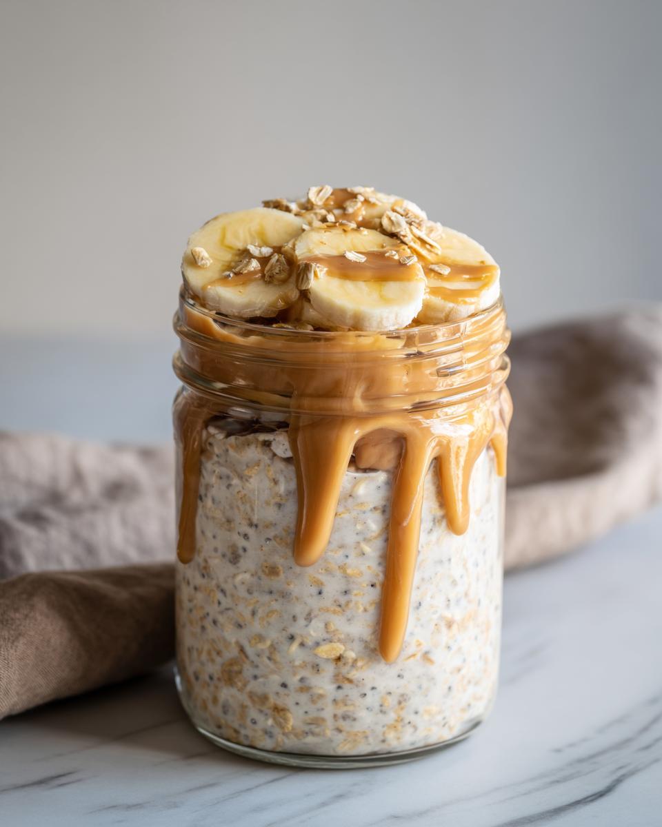 Peanut butter banana overnight oats in a glass jar topped with banana slices and peanut butter drizzle