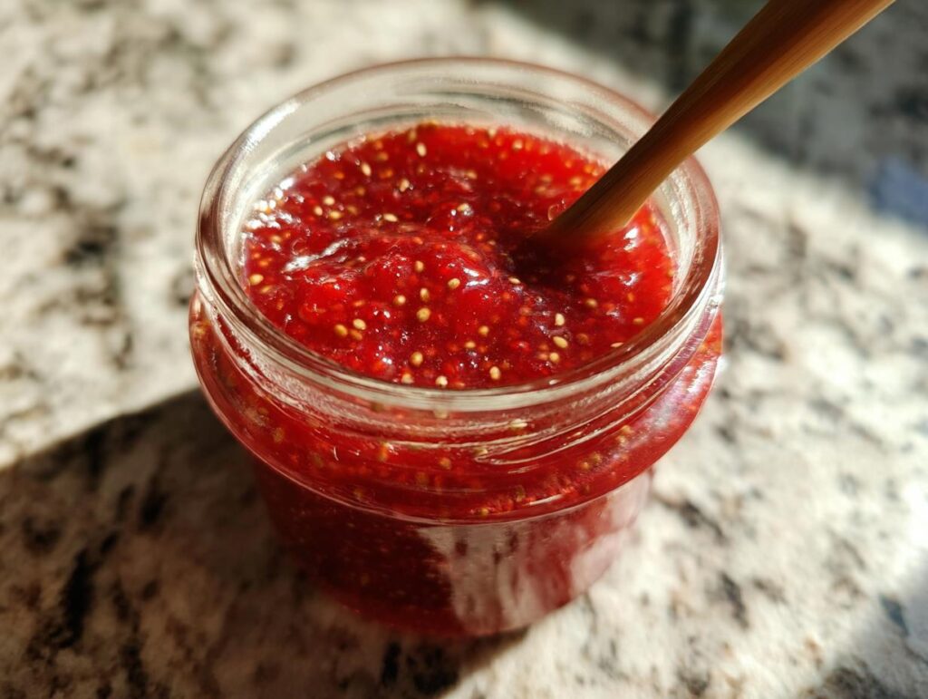 Close-up of a jar filled with homemade strawberry chia jam dessert topping with a wooden spoon inside.