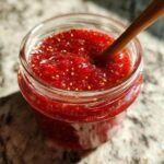 Close-up of a jar filled with homemade strawberry chia jam dessert topping with a wooden spoon inside.