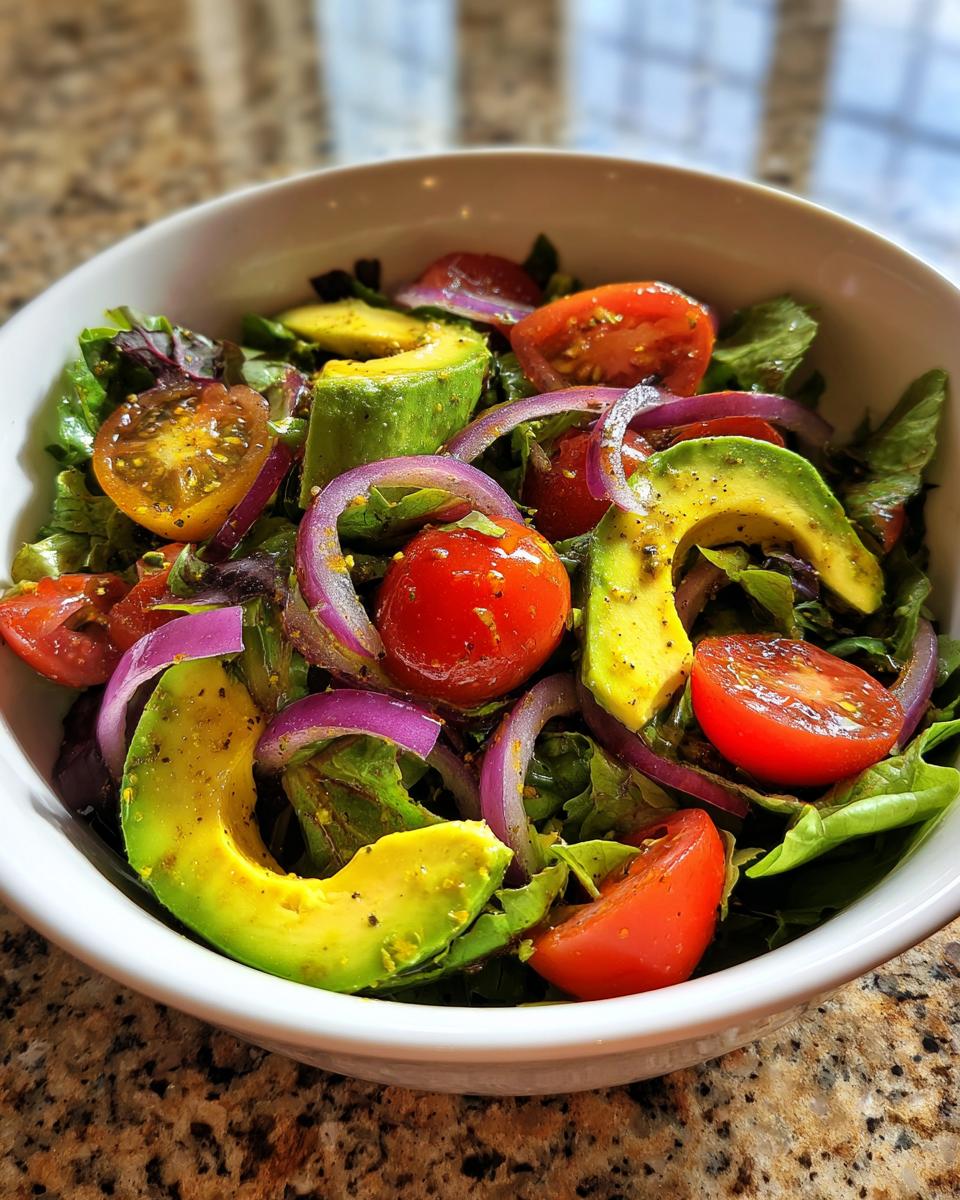 Bowl of fresh salad with avocado slices, cherry tomatoes, red onion, and leafy greens for lunch ideas healthy