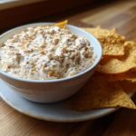 White bowl filled with creamy dip served with tortilla chips on a plate, perfect super bowl snacks