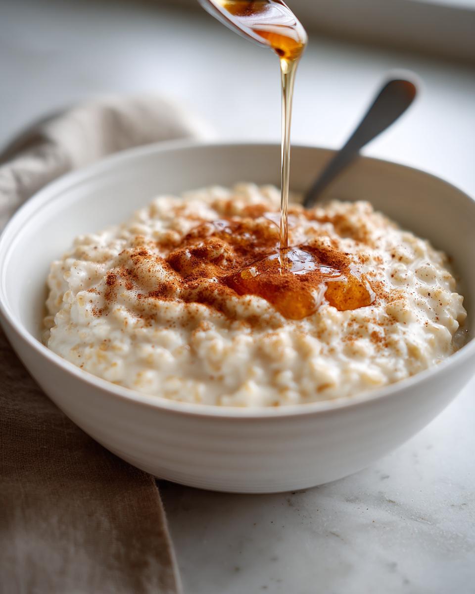 Bowl of creamy oatmeal topped with cinnamon and honey being drizzled from a spoon