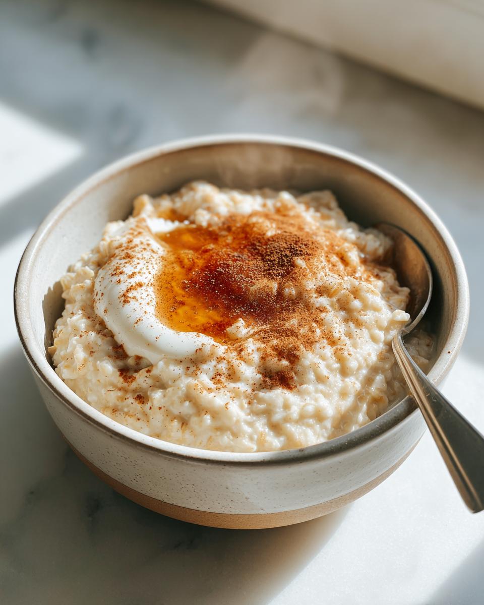 Bowl of creamy oatmeal topped with yogurt, honey, and cinnamon powder with a spoon.