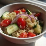 Quinoa bowl recipes with cherry tomatoes, cucumber, and red onion in a white bowl.