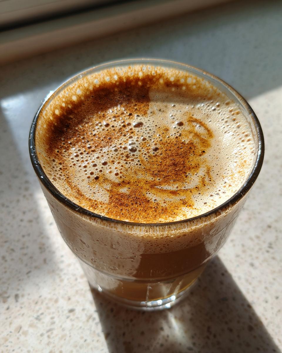 Close-up of a frothy date and banana smoothie suhoor topped with cinnamon in a clear glass.