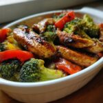 Grilled chicken strips with broccoli and red bell peppers in a white dish, keto dinner ideas