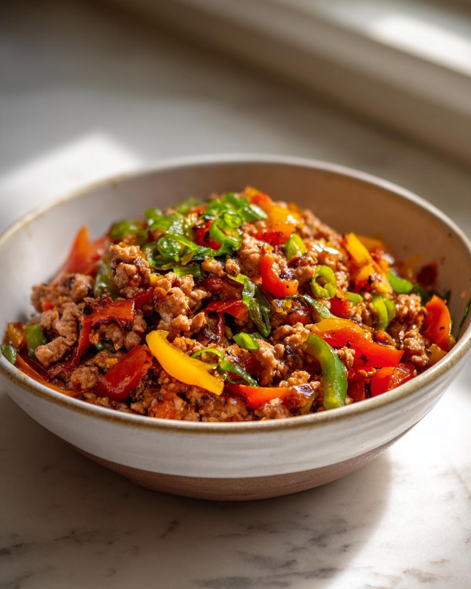 Bowl of ground turkey stir-fry with red, yellow, and green bell peppers, garnished with green onions.