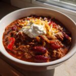Bowl of super bowl chili topped with shredded cheese and sour cream on a windowsill