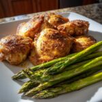 Plate of pan-seared chicken thighs with seasoned crispy skin served with grilled asparagus.