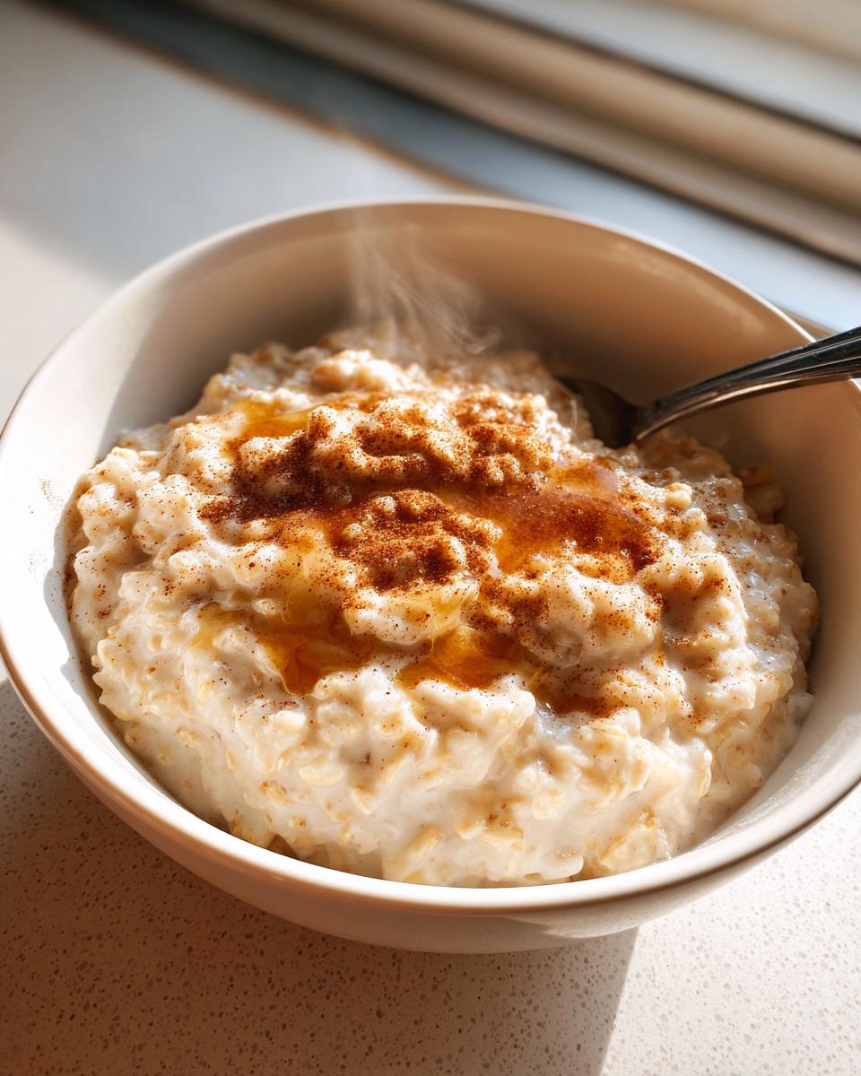 Bowl of steaming oatmeal topped with cinnamon and syrup on a countertop.