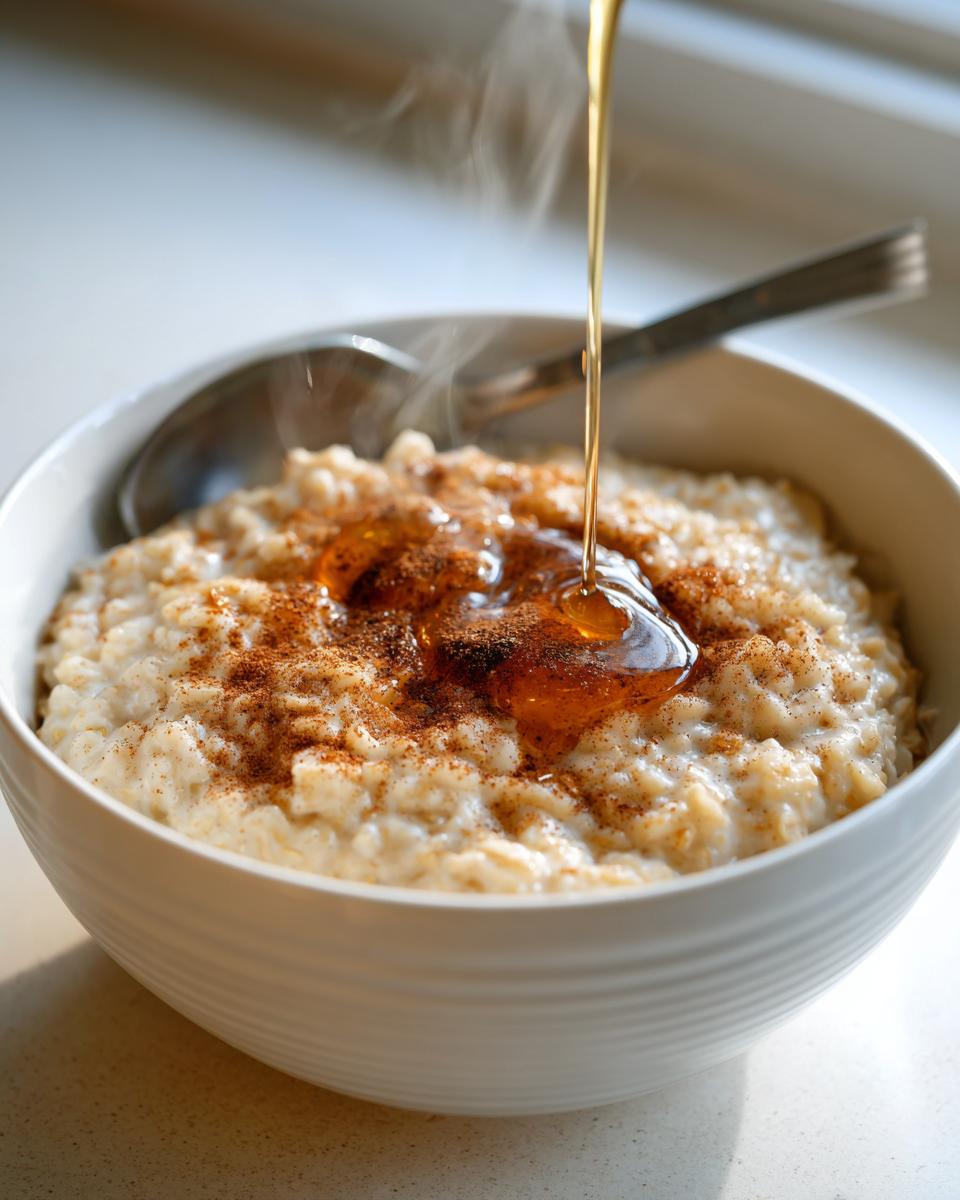 Steaming bowl of oatmeal with cinnamon and honey being drizzled on top