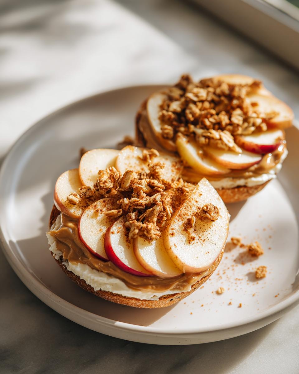 Bagel halves topped with cream cheese, peanut butter, apple slices, and granola on a plate, perfect after school snack recipes.