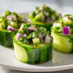 Close-up of avocado cucumber salad cups with red onion and herbs on a white plate.