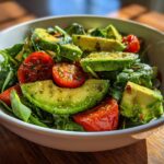Bowl of fresh avocado and cherry tomato salad with greens, seasoned and dressed.