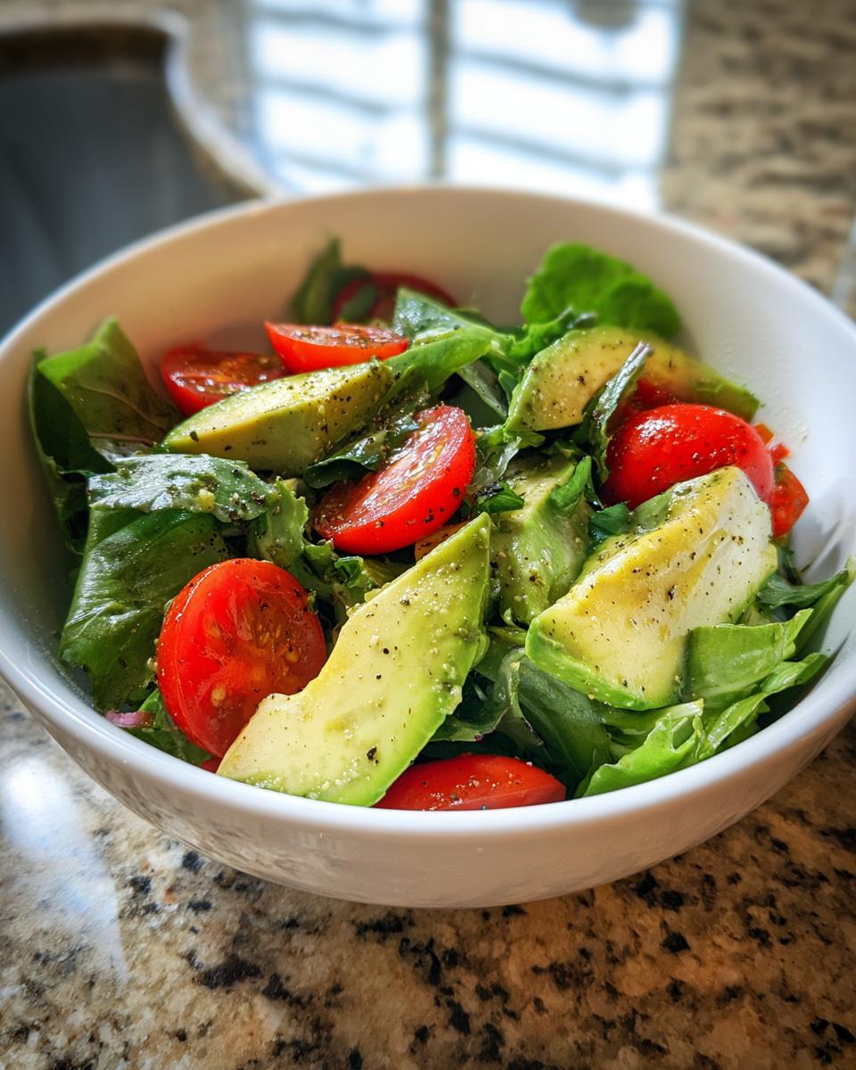 Bowl of fresh salad with avocado slices, cherry tomatoes, and leafy greens seasoned with pepper