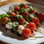 Caprese salad skewers appetizer with cherry tomatoes, mozzarella, basil, and balsamic glaze on a white plate.