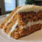 Close-up of a slice of carrot cake with cream cheese frosting on a white plate.