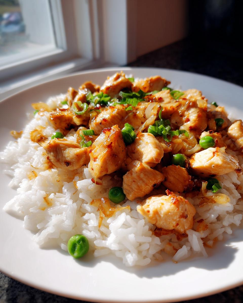 Plate of cooked chicken pieces with white rice and green peas garnished with chopped green onions
