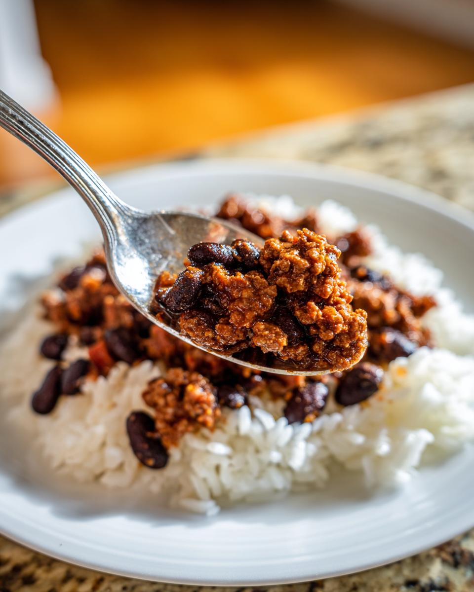 Close-up of a spoonful of chili with beans over white rice on a plate, budget friendly meals