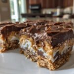 Two chocolate coconut dessert bars with layered chocolate, caramel, and coconut on a white plate.