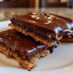 Two chocolate covered graham squares stacked on a white plate with glossy chocolate topping
