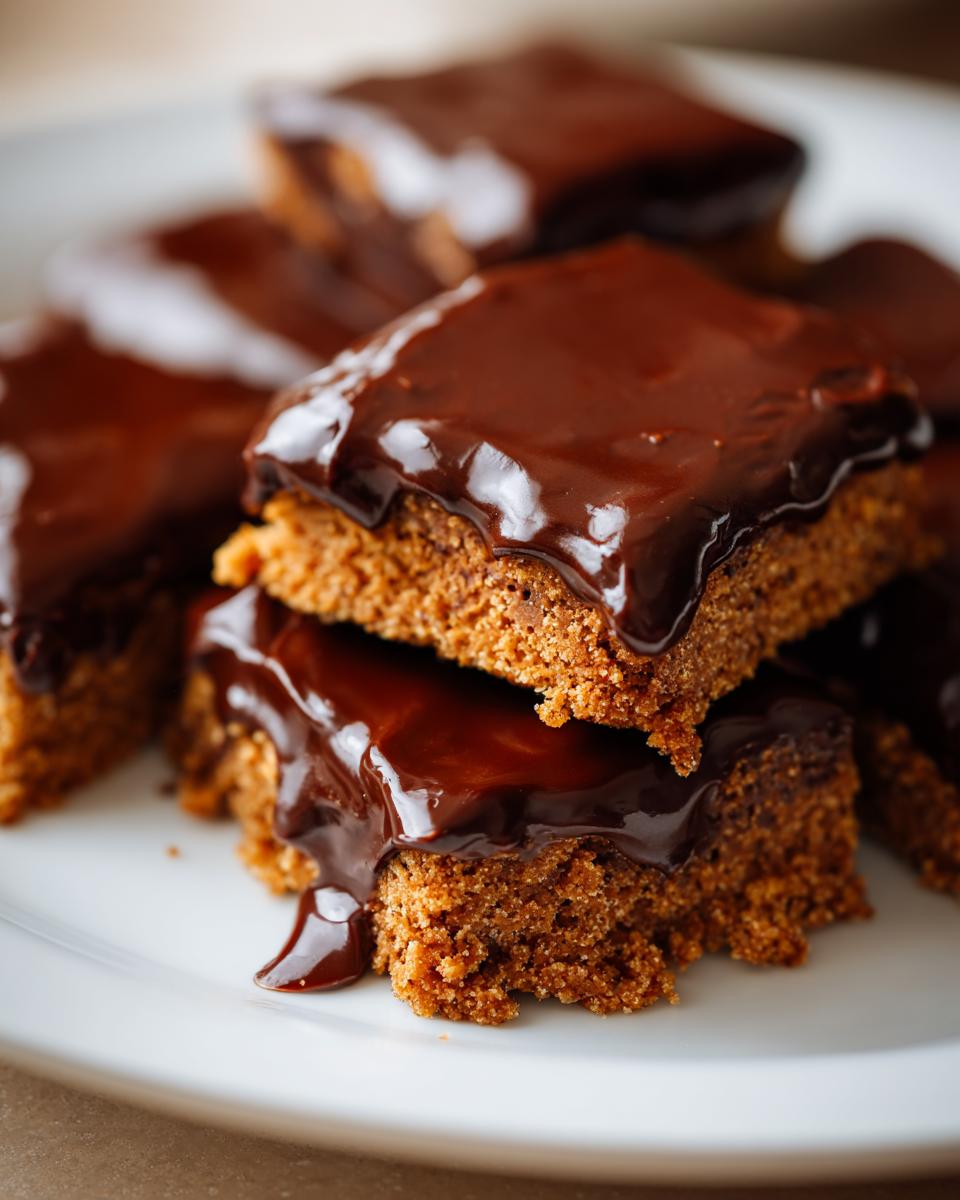 Stacked chocolate covered graham squares with glossy chocolate topping on a white plate.