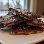 Stack of chocolate graham cracker bark pieces on a white plate with sprinkled sugar crystals.