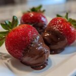 Three fresh strawberries dipped and stuffed with smooth melted chocolate on a white plate.