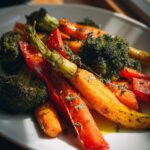 Plate of roasted vegetable recipes including carrots, broccoli, and red peppers garnished with herbs.