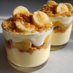 Two creamy banana pudding cups topped with banana slices and crumb topping in clear glass cups.