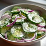 Bowl of creamy cucumber dill salad with sliced cucumbers, red onions, and fresh dill.