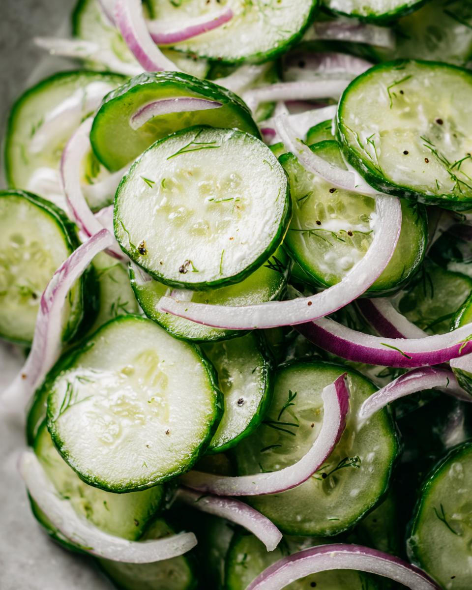 Close-up of creamy cucumber dill salad with sliced cucumbers and red onion rings.