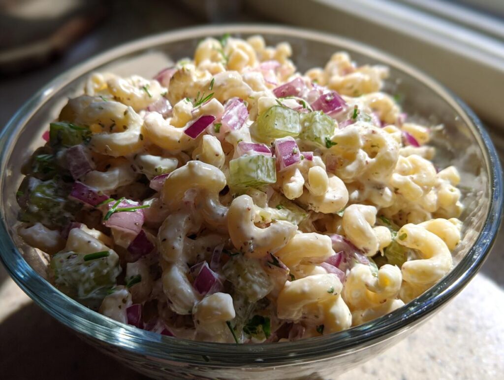 Close-up of creamy dill pickle pasta salad with elbow macaroni, diced pickles, red onion, and herbs.