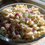Close-up of creamy dill pickle pasta salad with elbow macaroni, diced pickles, red onion, and herbs.