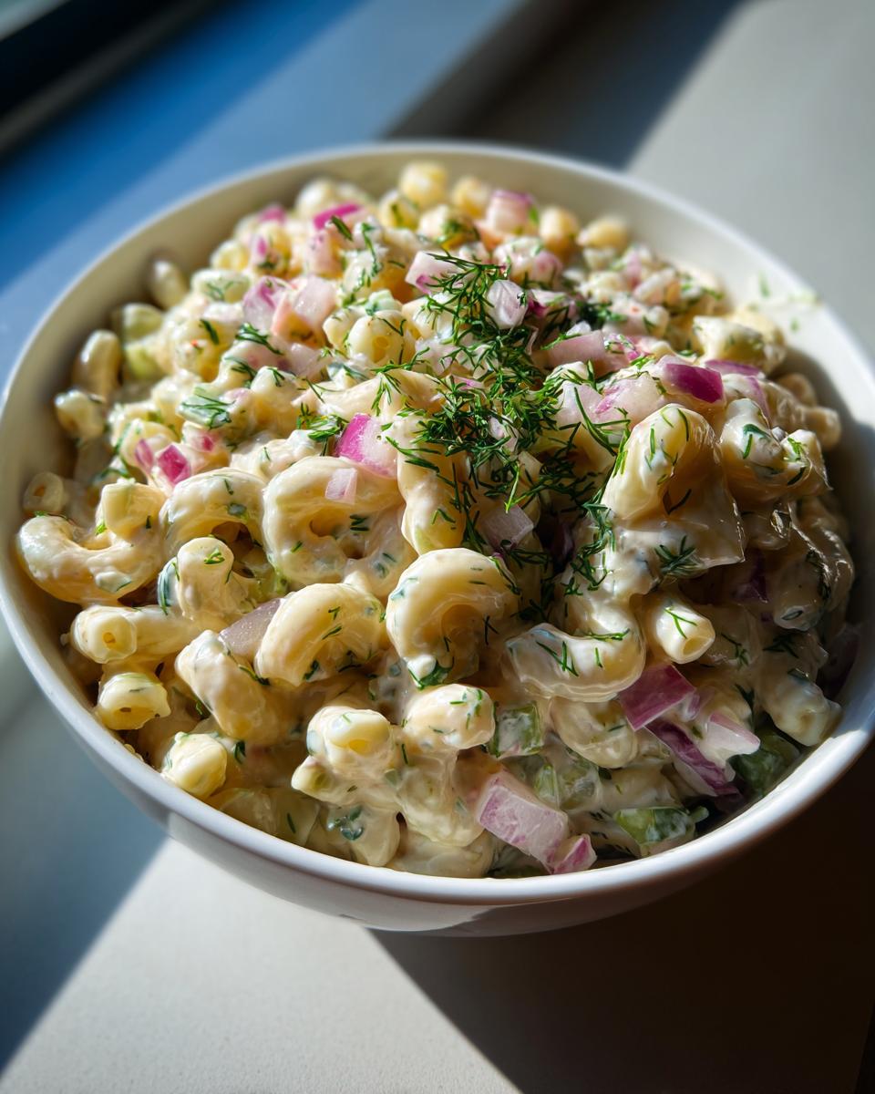 Bowl of creamy dill pickle pasta salad with macaroni, red onions, and fresh dill