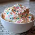 White bowl filled with creamy Funfetti dessert dip topped with colorful sprinkles.
