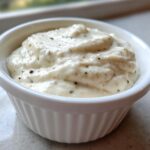 Close-up of creamy white dip with herbs in a white ramekin bowl on countertop.